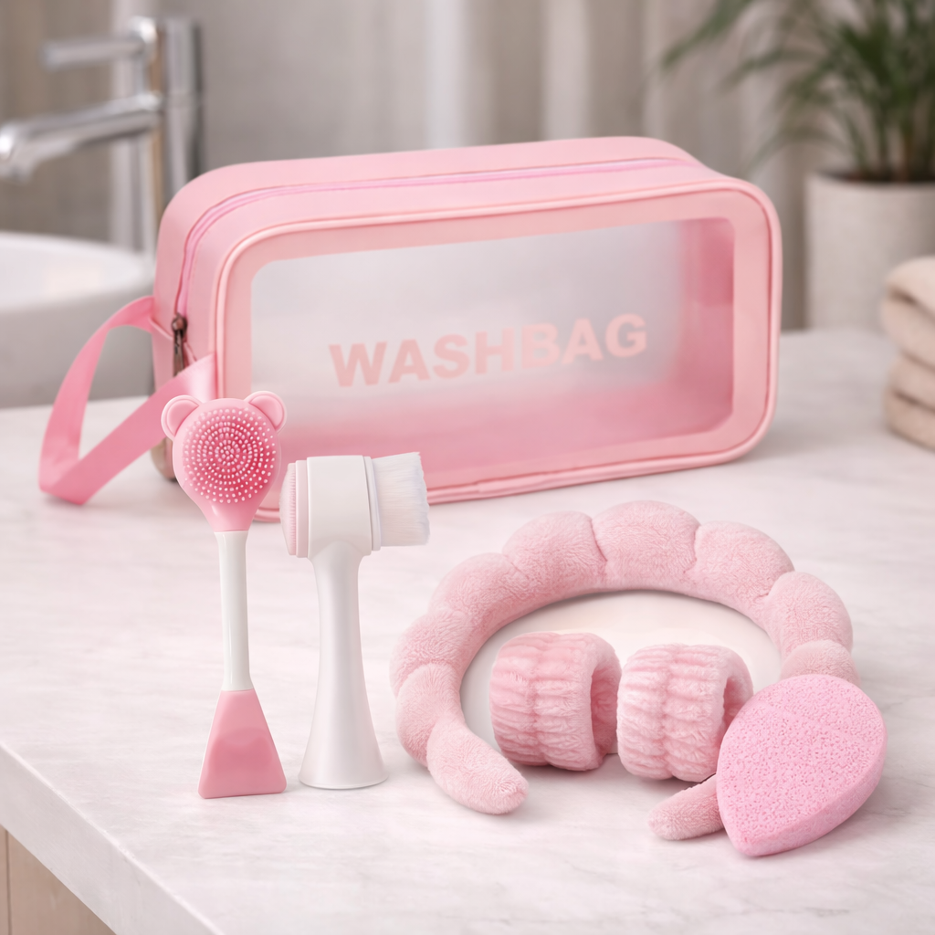 Set complet d’accessoires de soin visage rose avec trousse transparente Washbag, bandeau, brosse nettoyante et éponge exfoliante posés sur une table de salle de bain